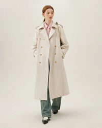 Woman city-strolling in a sand-beige double-breasted office long trench coat, 65 % poly / 35 % cotton twill and removable belt give timeless polish—your wind-proof 55-70 °F spring-fall commuter layer.