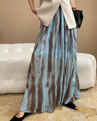 Discover our sheer pleated maxi skirt with abstract watercolor print, high-waisted fit, and flowy silhouette. 
