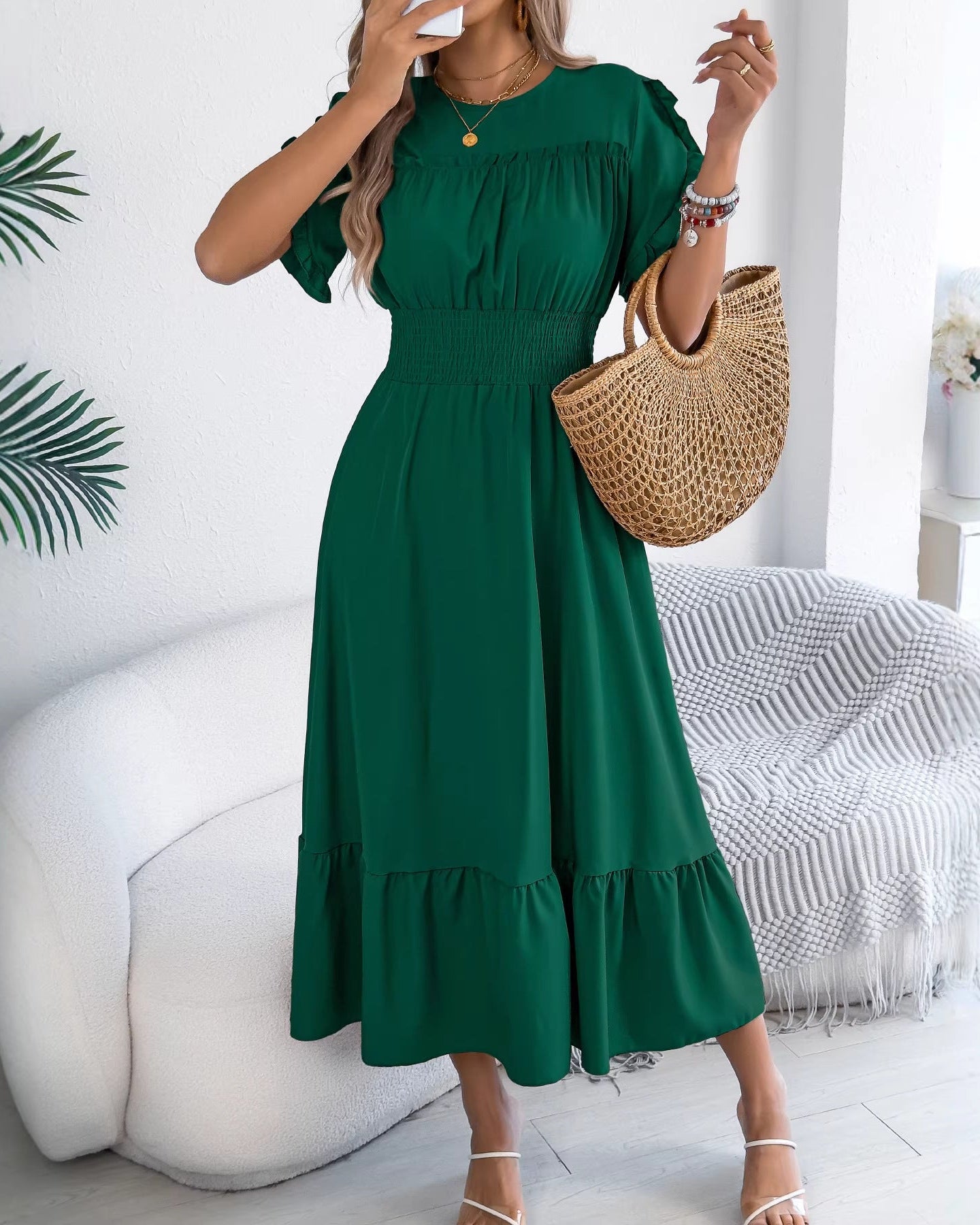 Model wearing ruffle trim short sleeve midi dress with shirred waist and tiered hem, carrying woven straw handbag, white strappy sandals, indoor cozy setting.