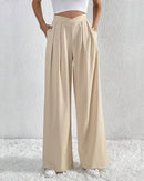 Model wearing high waist wide leg pants with crossover waist detail, paired with white cropped top and white sneakers.