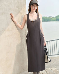 Woman strolling a weekend market in a sage-green pinch-pleat pocket dress, airy organic cotton and deep side pockets pair utility with feminine flow for hot-summer comfort.