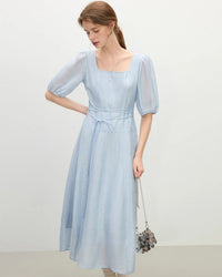 A romantic French-style dress with elegant puff lantern sleeves, a distinctive square neckline, and a lace-up detail, flowing to a mid-calf length.