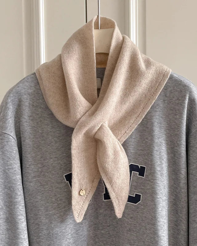  The triangular cut folds naturally around the neck, while a small circular accent adds subtle detail. 