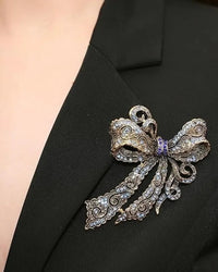 Baroque rhinestone bow brooch in silver tone, elegant metal pin with sparkling crystal accents and intricate ribbon design, perfect for adding glamour.