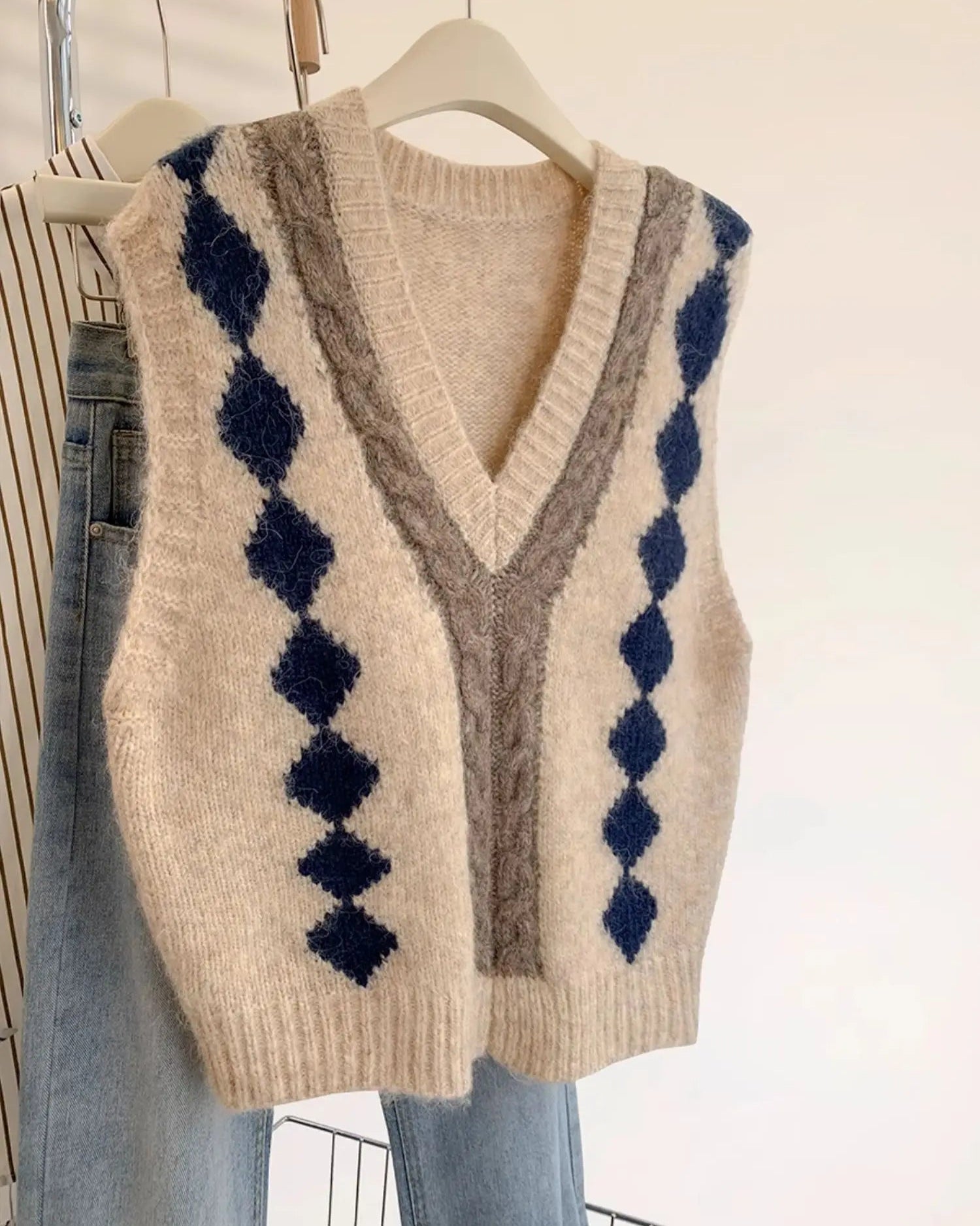A sleeveless knit sweater vest featuring a deep V-neck with contrast trim and a gingham pattern, offering a relaxed fit for effortless layering.