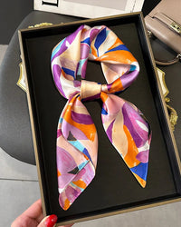 The scarf's smooth, featherlight construction makes it easy to style — draped at the collar, knotted through a bag handle, or worn as a headscarf.