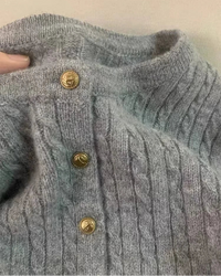 A pure cashmere cable-knit cardigan featuring a round neck, gold button closure, and a relaxed fit, crafted for elegant, layered warmth.