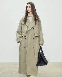 A floor-skimming trench coat with a turn-down collar, double-breasted front, and waist sash, designed for a relaxed, oversized silhouette.