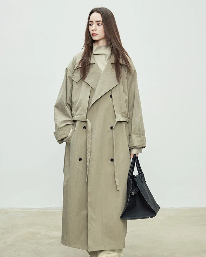 A floor-skimming trench coat with a turn-down collar, double-breasted front, and waist sash, designed for a relaxed, oversized silhouette.
