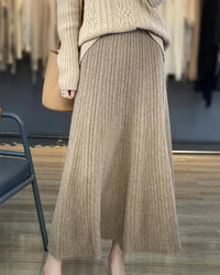A merino wool pleated A-line maxi skirt featuring a high waist, side pockets, and a fluid silhouette for elegant, warm comfort.