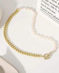 A necklace featuring natural baroque freshwater pearls on an asymmetric 14K gold-filled link chain with a cross motif, designed for a modern look.