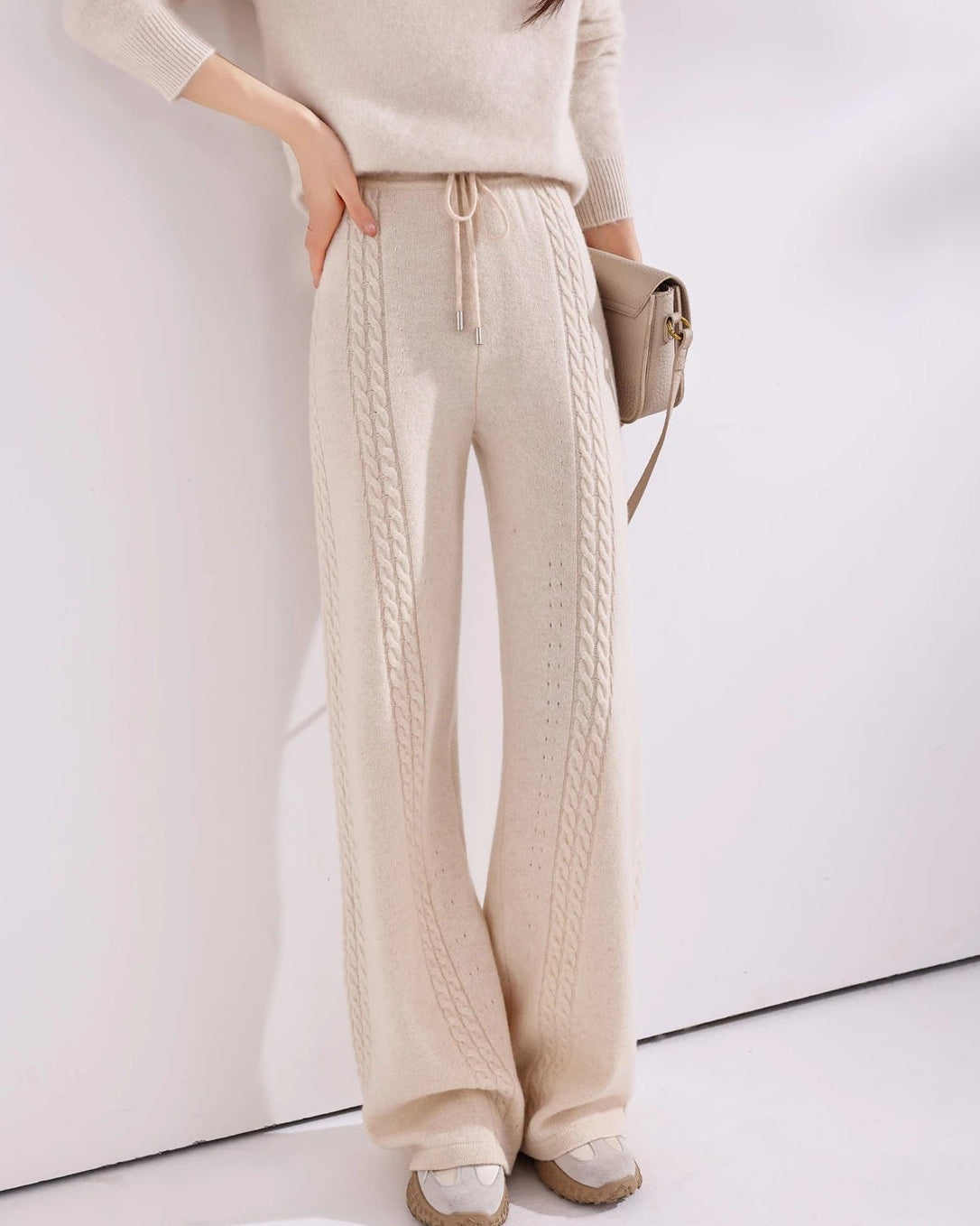 Cable-knit wool wide-leg pants for women with vertical cable panels, drawstring waist and full-length wide-leg shape, a warm fall-winter knit trouser for relaxed everyday wear.