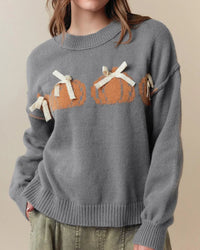 A pumpkin bow knit pullover with pumpkin and bow motifs, loose fit and long sleeves, designed for a cozy winter layering look that pairs from sneakers to boots.