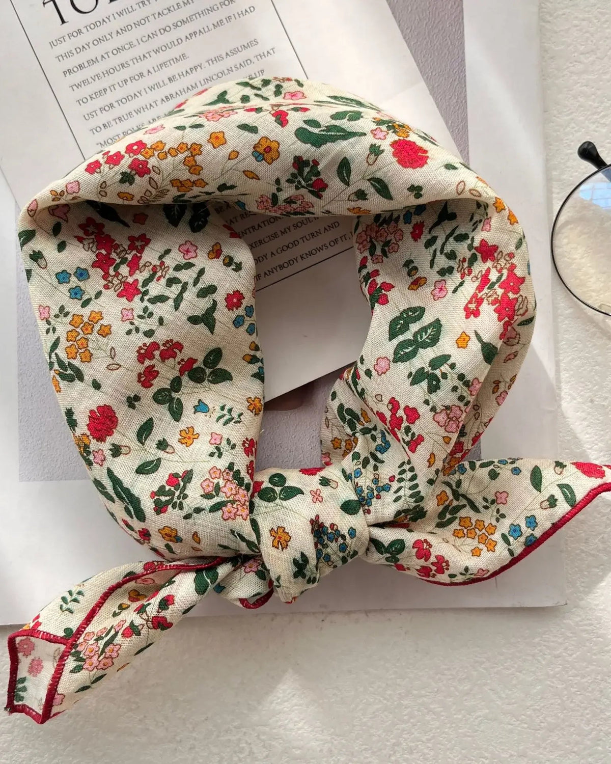 A small square scarf with a fine floral print and light smooth fabric, designed to knot at the neck, tie as a headband, or accent a bag.
